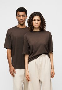 Καφέ μονόχρωμες μπλούζες από ελαφρύ ύφασμα, με κοντά μανίκια και άνετη εφαρμογή, σε συνδυασμό με ανοιχτό μπεζ, φαρδιά παντελόνια.