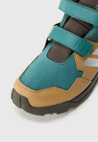 Sapatilha de caminhadas em turquesa e bege, feita de materiais em malha e borracha. Apresenta fechos de velcro, acabamento texturizado e uma sola de borracha resistente.