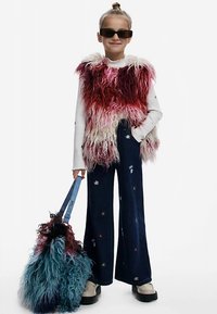 Vesta z umelého kožušiny v červených a ružových tónoch cez biely rebrovaný top, skombinovaná s tmavými širokými džínsami s kvetinovou výšivkou. Doplnok: chlpatá taška.