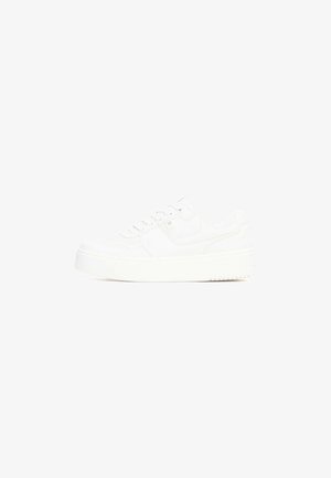 Zapatilla blanca con parte superior de cuero suave, puntera redondeada, cordones planos, cuello acolchado y suela gruesa de goma con dibujo texturizado.