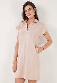 Robe polo de couleur rose clair, à manches courtes, fabriquée en tissu doux ; dotée d'un col retourné et de deux poches latérales pour la fonctionnalité.