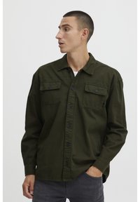 Camicia verde oliva con bottoni, dotata di due taschini sul petto, realizzata in tessuto morbido, con colletto classico e bottoni neri per la chiusura.