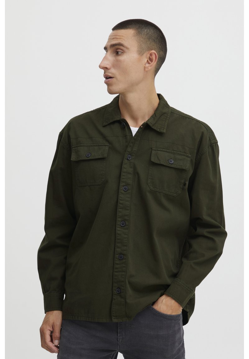 Camicia verde oliva con bottoni, dotata di due taschini sul petto, realizzata in tessuto morbido, con colletto classico e bottoni neri per la chiusura.