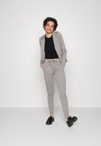 Fato cinza claro, sob medida, com um blazer ajustado e calças com cordão. Combinado com um top cropped preto e sapatos pretos. Tecido suave, design minimalista.