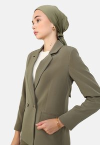 Blazer vert olive avec un double bouton, design ajusté, revers à cran et deux poches avant. Accompagné d'un foulard assorti.