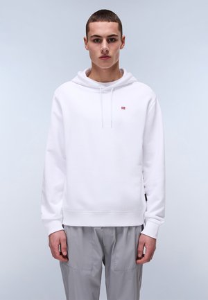 Hvid hættepullover med snøre i hætten, med et lille rødt logo på brystet, parret med lysegrå bukser. Stoffet ser glat og blødt ud.