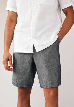 Linen short-sleeve white shirt with buttoned front and small chest pocket, paired with dark gray linen shorts featuring a textured weave.