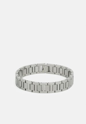 Bracelet en métal avec des maillons rectangulaires, présentant une surface texturée et une finition brillante. La couleur est argentée, avec un fermoir sécurisé pour la fermeture.