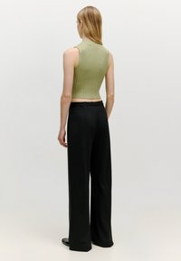 Grünes geripptes Crop-Top und schwarze weit geschnittene Hose. Das Top hat ein figurbetontes Design, während die Hose eine glatte Textur und einen taillierten Schnitt aufweist.