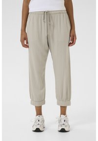 Light beige, loose-fitting pants with an elastic waistband, drawstring, and elastic cuffs. Fabric appears soft with a smooth texture.
