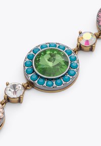Un bracciale multi-pietra con una grande pietra verde sfaccettata circondata da accenti turchesi e rosa, montato in metallo color oro.