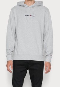 Felpa grigia in cotone con tasca frontale, cappuccio regolabile con cordino e logo ricamato "TOMMY JEANS" in blu scuro e rosso.