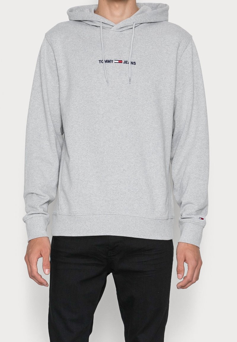 Felpa grigia in cotone con tasca frontale, cappuccio regolabile con cordino e logo ricamato "TOMMY JEANS" in blu scuro e rosso.