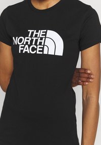 Svart t-shirt med kort ärm som har en stor vit logotyp "THE NORTH FACE" över bröstet. Tillverkad av ett slätt tyg med en åtsittande design.