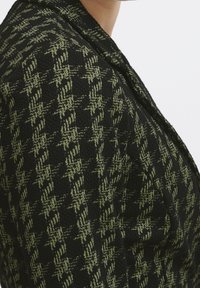 Blazer nero e verde con trama a motivo pied de poule, caratterizzato da un colletto a revers e dettagli di cuciture visibili.