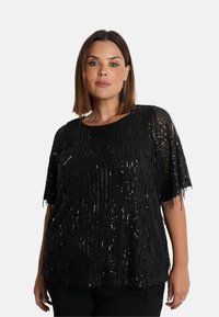 Svart paljettopp med fransdetaljer, korta ärmar och rundad halsringning. Har en strukturerad, lager-på-lager-design med en glänsande finish.