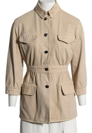 Beige langærmet jakke med sorte knapper, fire klaplommer, en krave og indsnævring i taljen vist på en hvid mannequin.