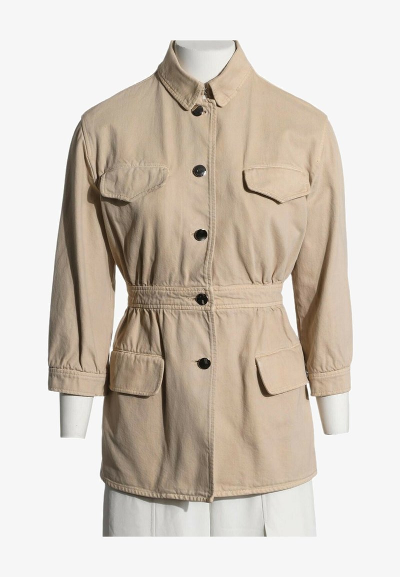 Veste beige à manches longues avec boutons noirs, quatre poches à rabat, un col et une taille cintrée, présentée sur un mannequin blanc.