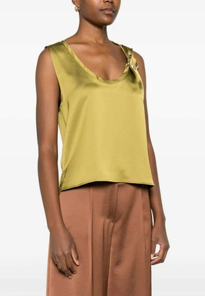 Donna che indossa un top smanicato verde oliva lucido con un dettaglio di fibbia metallica sulla spalla sinistra, abbinato a pantaloni marroni a vita alta.