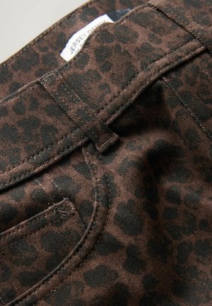 Braun gepunkteter Leopardendruckstoff mit dunklen Flecken, versehen mit Steppdetails und einem Etikett am Bund. Strukturiertes Material mit sichtbaren Nähten und Taschen.