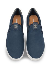 Zapatillas azul marino de tipo slip-on con una textura suave, suela de goma blanca y un pequeño logo en la parte del empeine. Forradas con un color claro en contraste.