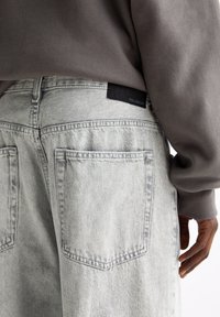 Light grey denim pants with two back pockets, accompanied by a grey sweatshirt. Features a black fabric label on the waistband.