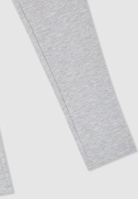Gamba di pantalone in tessuto grigio chiaro con cuciture visibili su uno sfondo chiaro uniforme.