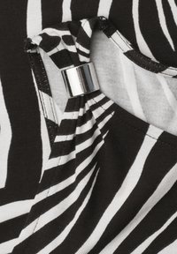 Gros plan d’un tissu rayé noir et blanc avec un fermoir cylindrique argenté retenant le tissu froncé près d’une couture d’encolure.