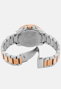 Hõbe roostevaba terasest kell roosa kuldse aktsendiga kellakorpuse ja randme säärega. Omab klamberkinnitust, ümmargust korpust ja siledat tagakülge.