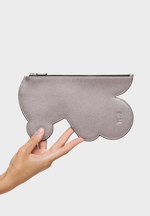 Mano sosteniendo un clutch metálico plateado con textura, de forma abstracta y ondulada, con una cremallera negra en la parte superior.