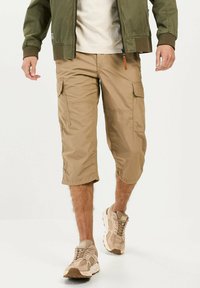 Beige cargo shorts med knælængde, med sidelommer og en glat overflade, parret med lyse beige sportssko.