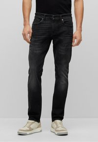 Jeans in denim scuro con vestibilità slim, caratterizzati da una leggera scoloritura, design a cinque tasche e cuciture a contrasto; abbinati a sneaker chiare.