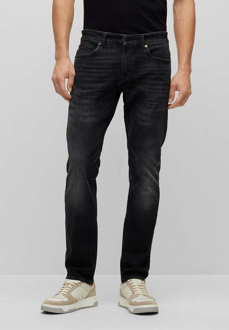 Jeans in denim scuro con vestibilità slim, caratterizzati da una leggera scoloritura, design a cinque tasche e cuciture a contrasto; abbinati a sneaker chiare.