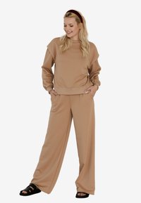 Beżowa bluza i szerokie spodnie, wykonane z miękkiego materiału. Bluza ma wysoki kołnierz i opadające ramiona, podczas gdy spodnie mają elastyczny pas.