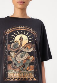 Sort bomulds t-shirt med et iøjnefaldende grafisk design med slanger, blomster og solmotiver i jordfarver. Løs pasform med korte ærmer.