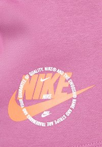 Nike-grafisk sweatshirt i ljusrosa med en orange logotyp och cirkulär textdesign. Tyget har ett strukturerat, stickat utseende.