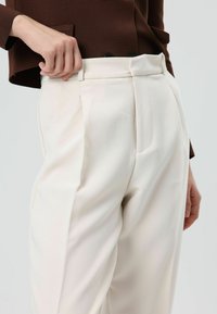 Witte op maat gemaakte broek met een gladde textuur, voorzien van voorplooien, een hoge taille en een zijzak, gecombineerd met een bruin topje.