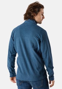 Blå fleecepullover med hög krage och långa ärmar, med en texturerad tyg och sömmar längs axlarna och sidorna.