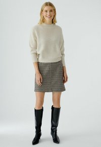 Helle beige gerippte Pullover, hoher Kragen, kombiniert mit einem schwarz-weißen Hahnentrittmuster-Minirock und knielangen schwarzen Lederstiefeln.