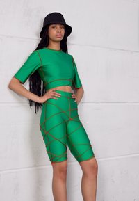 Conjunto verde de duas peças, com um top cropped de mangas curtas e calções de cintura alta. Embelezado com costuras laranjas em cruz.