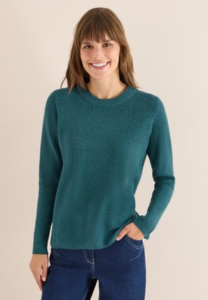 Türkisfarbener Strickpullover mit Rundhalsausschnitt und langen Ärmeln, der ein strukturiertes Muster aufweist. Kombiniert mit dunkelblauen Jeans.
