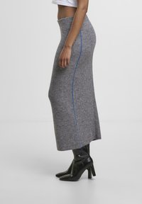 Grauer gerippter Strickrock mit hoher Taille und seitlichem Schlitz, der über eine kontrastierende blaue Naht verfügt. Getragen mit schwarzen Absatzstiefeln.