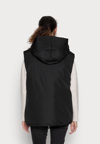 Schwarze ärmellose Steppweste mit Kapuze, mit einer glatten, glänzenden Oberfläche, elastischem Saum und ohne sichtbare Verschlüsse. Schlichte Rückansicht.