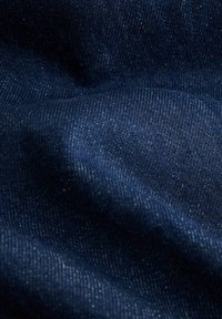 Tamno plavi denimski materijal s teksturiranom površinom, s blagim uzorkom tkanja i laganim sjajem, koji pokazuje mekoću i fleksibilnost.