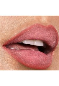 Matte nude lippenstift aangebracht op volle lippen, met een gladde textuur en subtiele glans, waarbij de natuurlijke liplijn zichtbaar is en witte tanden ertussen zichtbaar zijn.