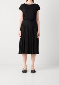 Mustat lyhythihaiset paita yhdistettynä pleatattuun mustaan midi-hameeseen. Hameessa on teksturoitu pinta ja se istuu korkealla vyötäröllä, jota täydentävät mustat ballerinat.