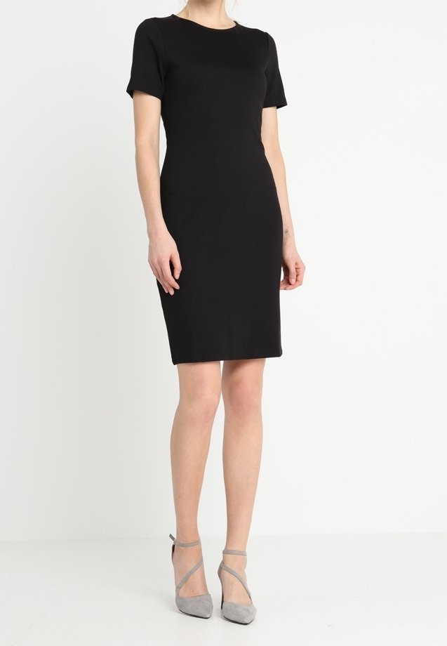 Robe noire ajustée avec des manches courtes, encolure ronde, ourlet à mi-genoux, texture lisse, associée à des chaussures à talons hauts à lanières grises.