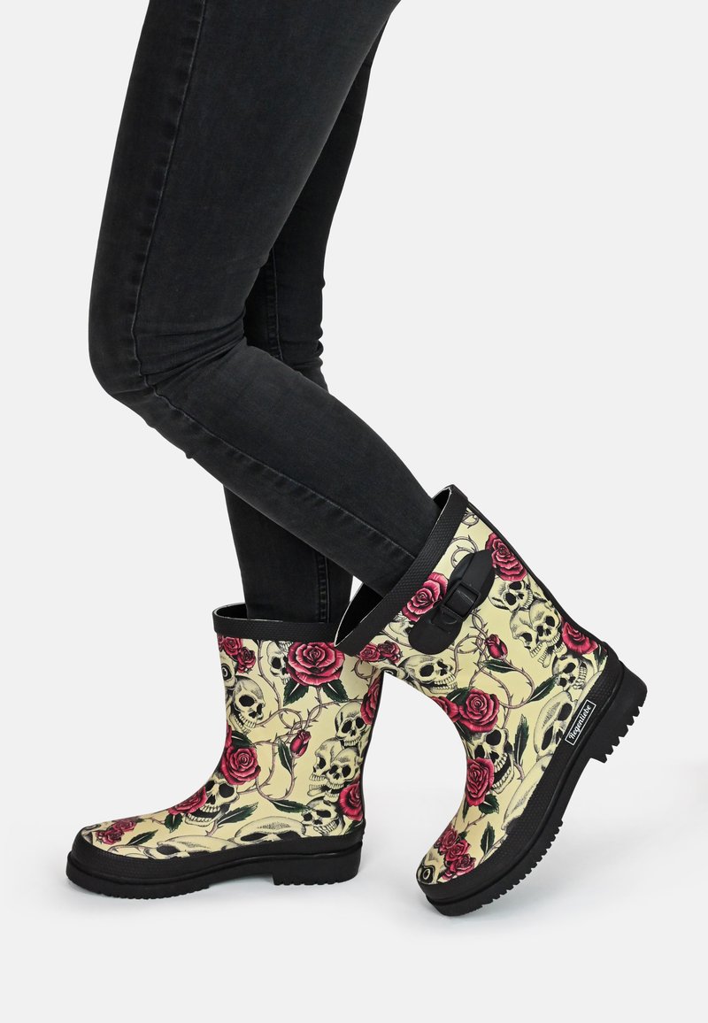 Schwarze Gummi-Regenstiefel auf gelbem Hintergrund, verziert mit roten Rosen und Totenkopf-Mustern sowie einem schwarzen Riemen-Akzent im oberen Bereich.