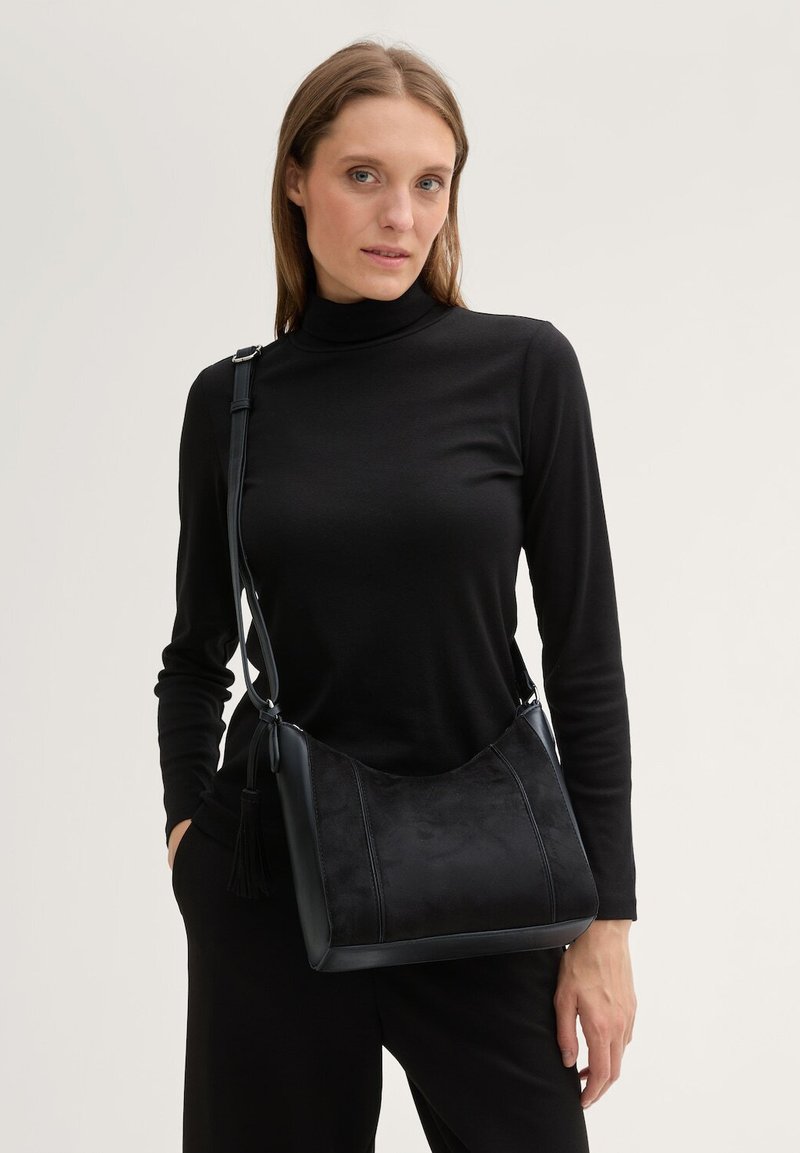 La borsa a spalla nera presenta un corpo in pelle liscia con un pannello frontale in suede opaco, base piatta e una tracolla regolabile con dettagli in nappina.