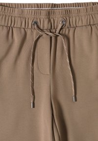 Hnědé tepláky s texturovanou tkaninou, elastickým pasem a nastavitelnou šňůrkou s metalickými konci, které mají boční kapsy.